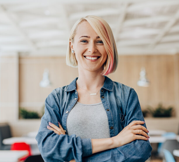 Woman stands in a conference room with arms confidently crossed and smiling.